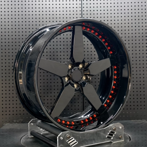 Angled workshop view of forged five-spoke wheel showing deep lip and red bolt details